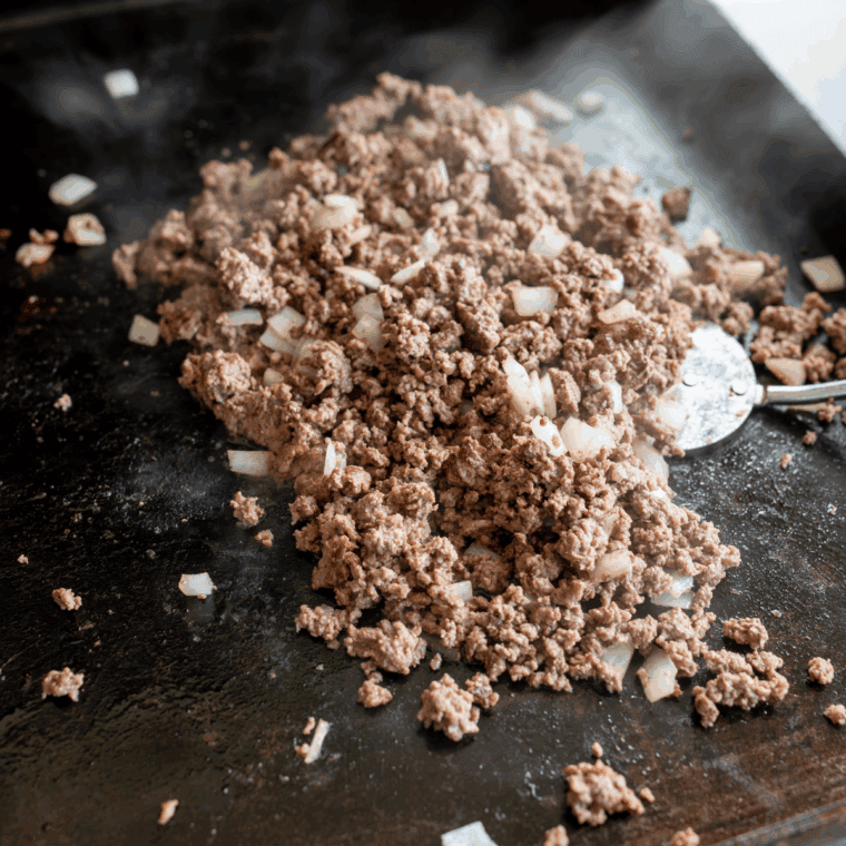 Cooking ground beef on the griddle and seasoning with spices until fully coated and flavorful.