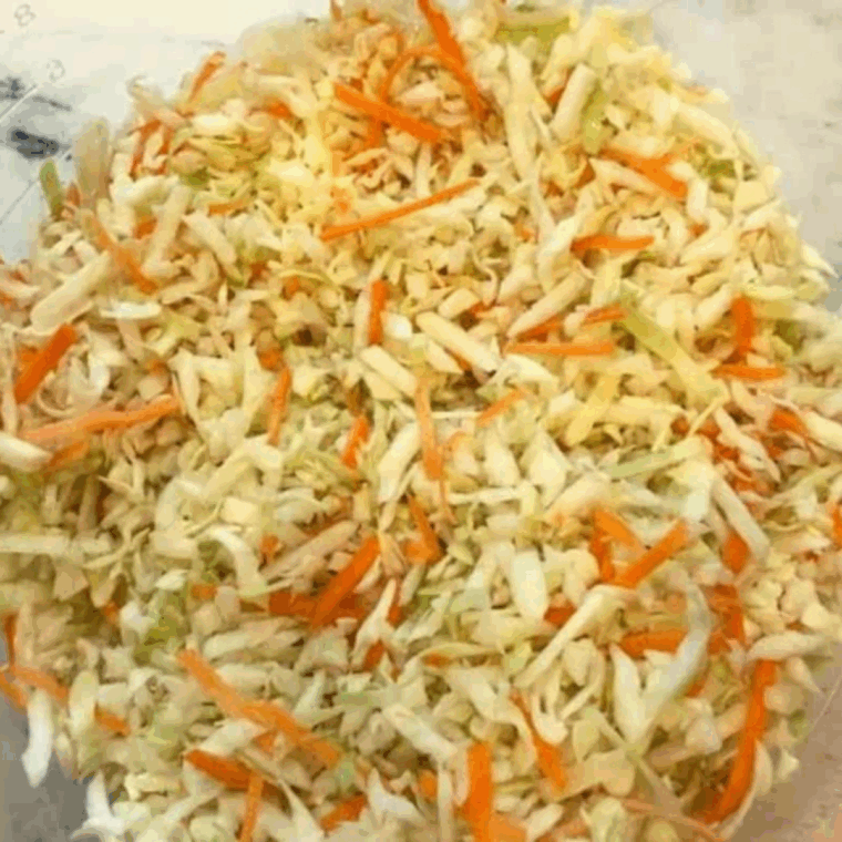 Shredded green cabbage and grated carrots placed in a large mixing bowl.