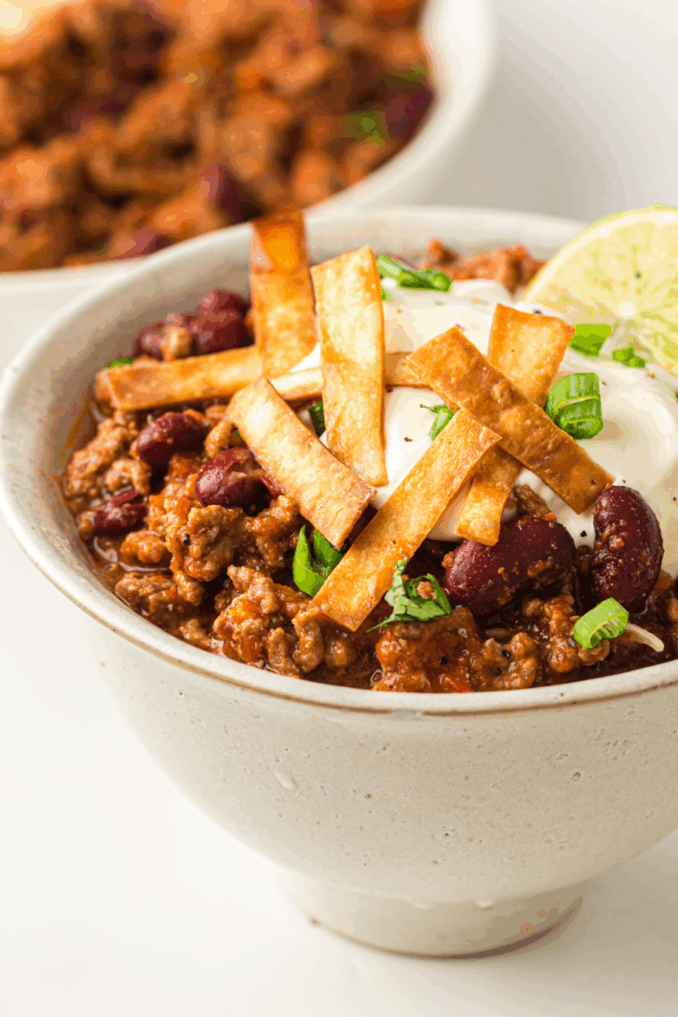 A steaming bowl of thick, beefy George’s Chili topped with shredded cheddar cheese and diced red onions, inspired by the classic Culver’s recipe and served with saltine crackers.