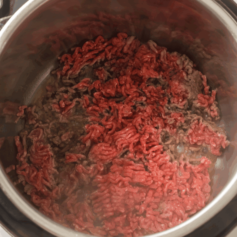 Browned ground beef and diced yellow onions cooking inside a stainless steel Instant Pot liner on the sauté setting.