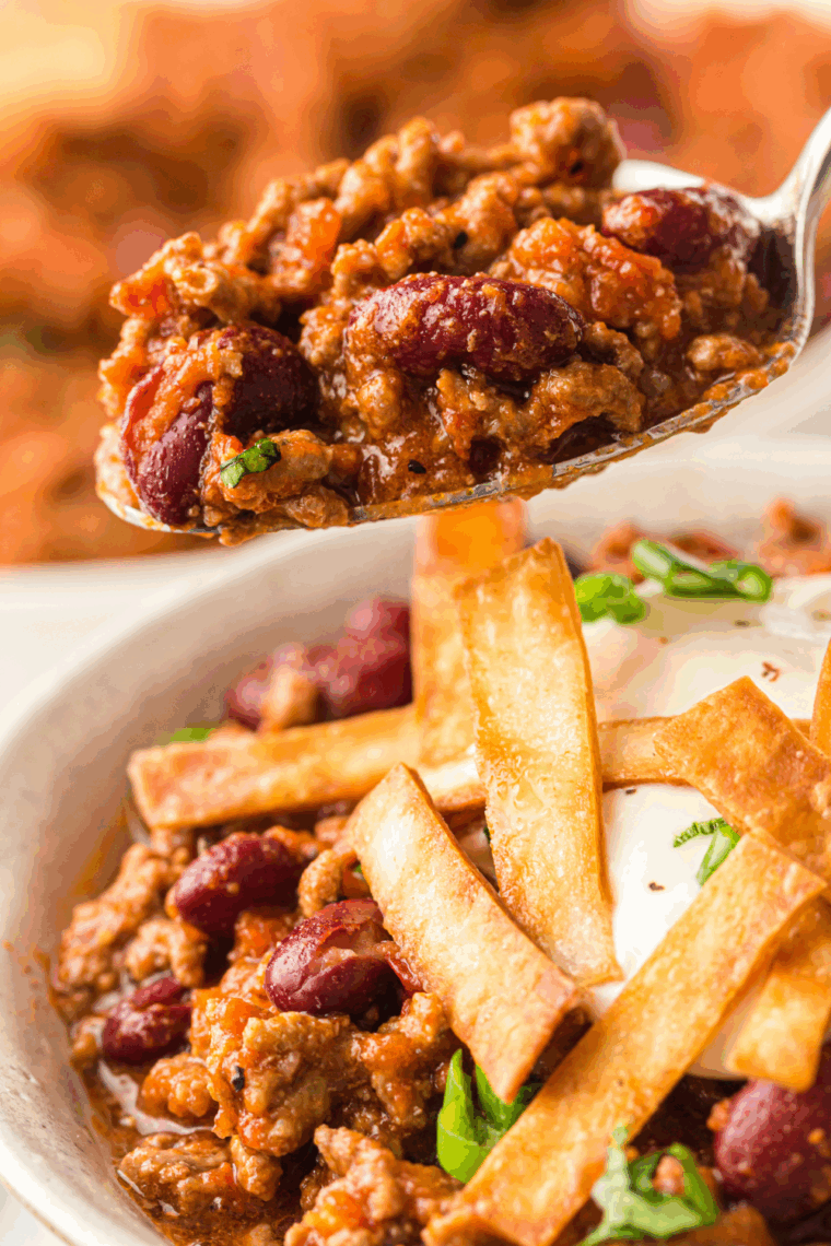 A steaming bowl of thick, beefy George’s Chili topped with shredded cheddar cheese and diced red onions, inspired by the classic Culver’s recipe and served with saltine crackers.