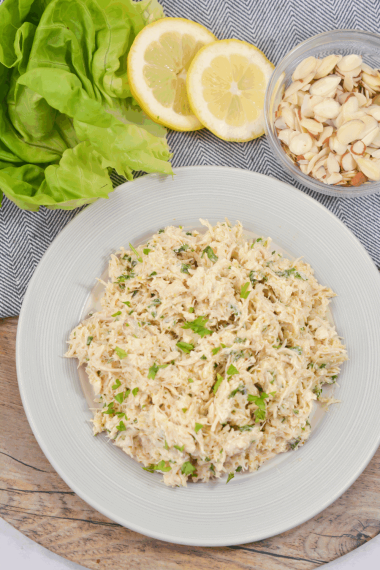 Creamy chicken salad made without celery, mixed with mayonnaise, pesto, fresh basil, lemon juice, and sliced almonds, ready to serve.