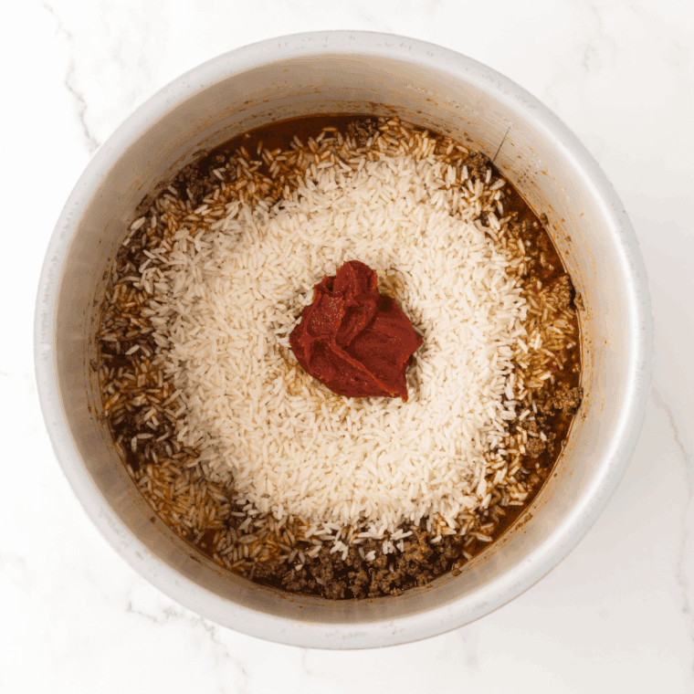 Adding diced onions, green peppers, and minced garlic to the browned meat in a skillet to sauté.