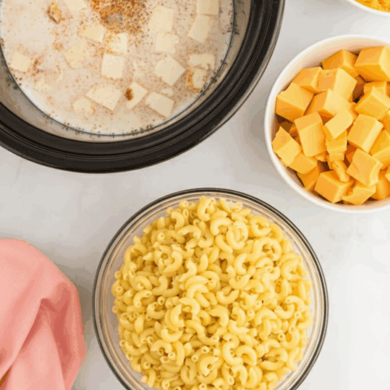 Pouring uncooked elbow macaroni, milk, heavy cream, and butter into a greased black slow cooker.