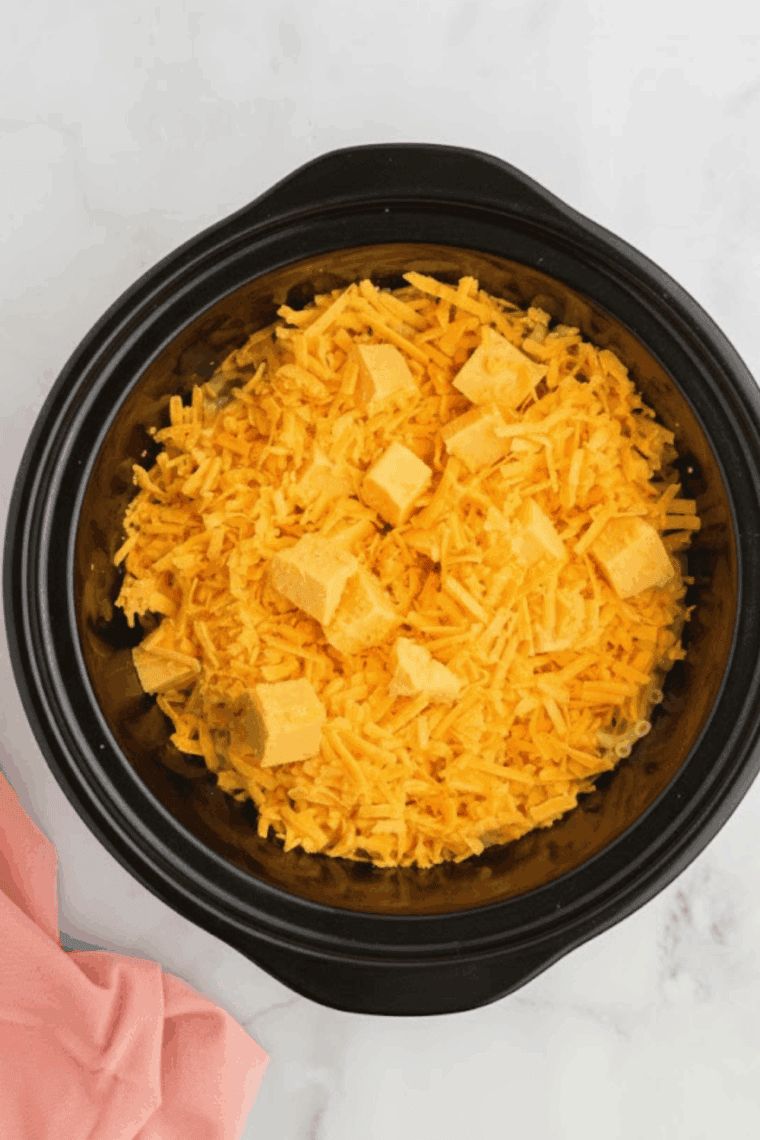 A black slow cooker with the lid on, simmering macaroni and cheese on the low heat setting.