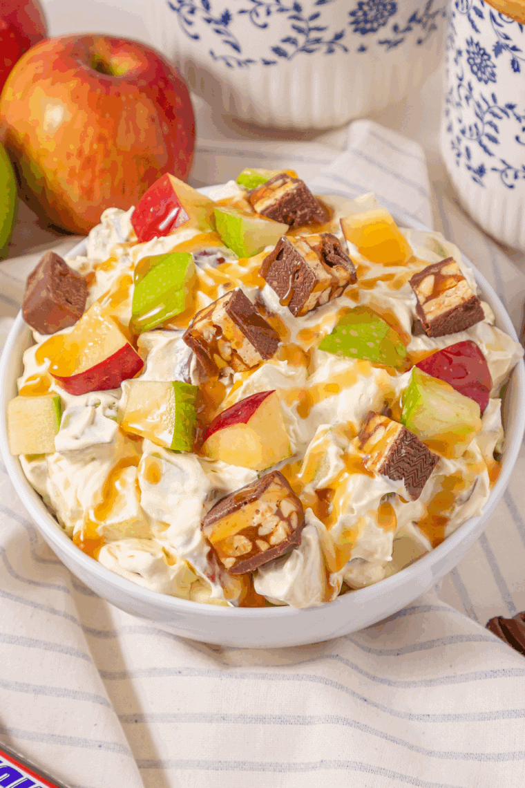 Bowl of Easy Candy Bar Apple Salad with diced apples, Snickers pieces, creamy pudding mixture, and caramel drizzle on top.