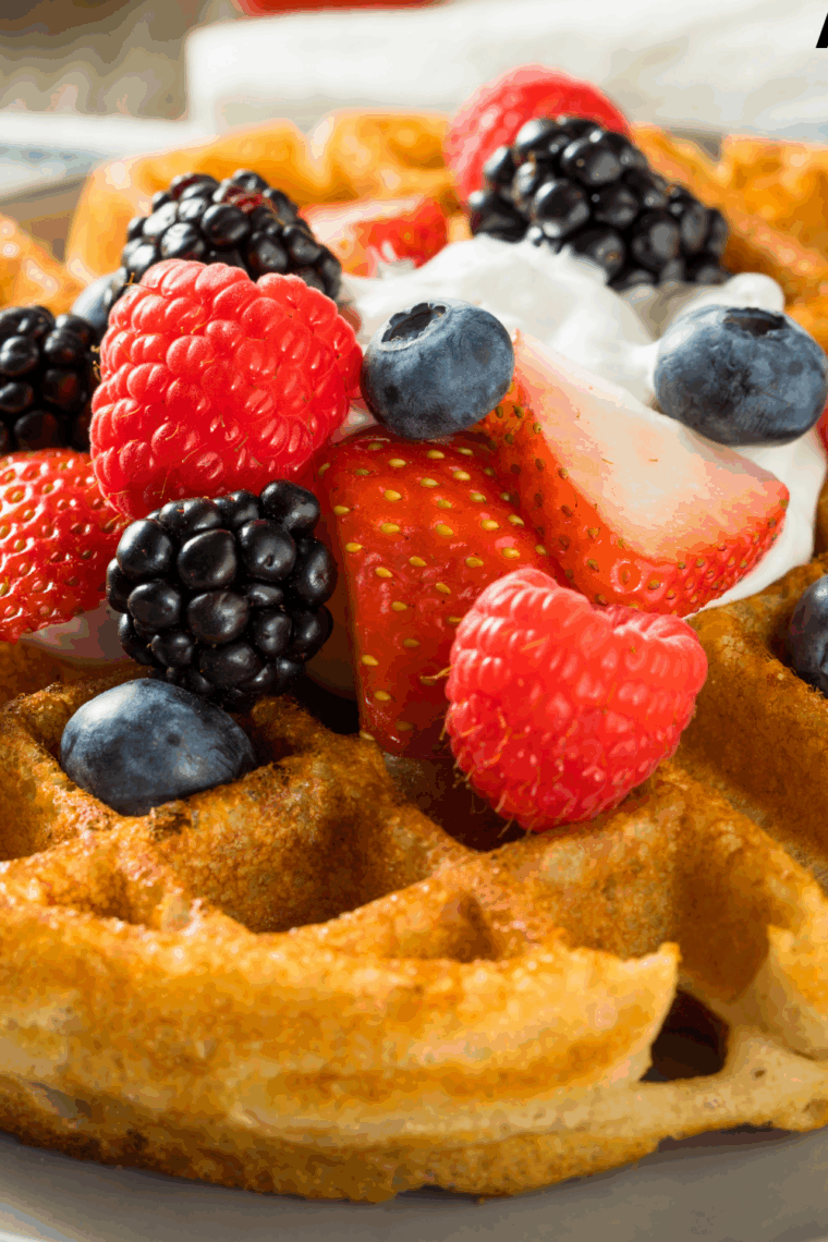 Golden, crispy First Watch-style waffles served on a plate with syrup and fresh berries.