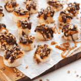 Frozen banana bites topped with chopped Snickers and drizzled chocolate, served on a plate