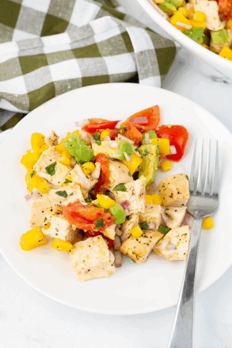 Fresh mango salad dressing in a bowl with a spoon, surrounded by mango pieces and lime wedges