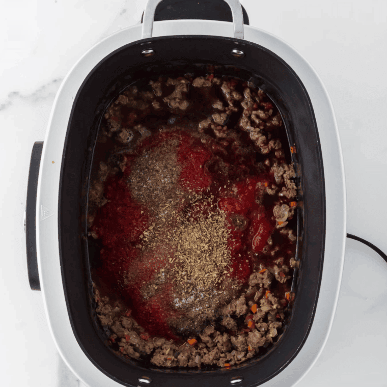 Adding meat and tomatoes to crockpot for slow cooker bolognese.