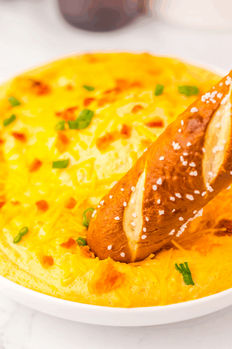 Slow Cooker Beer Cheese Dip with melted cheddar, cream cheese, and beer, topped with scallions and crumbled bacon, served in a small bowl with a spoon.