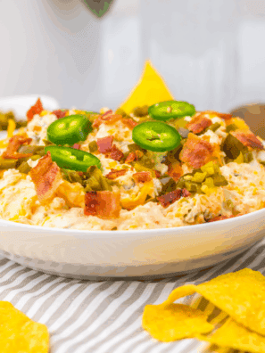 Slow cooker jalape&ntilde;o popper dip with cream cheese, melted cheddar, bacon, and sliced jalape&ntilde;os in a crockpot
