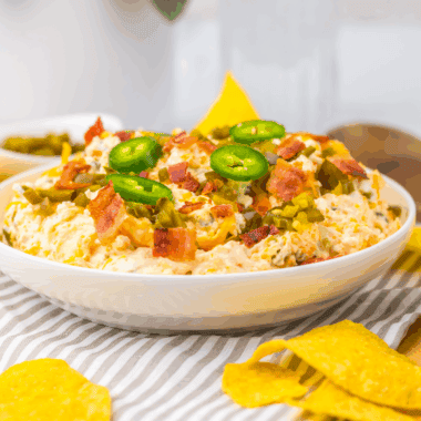 Slow cooker jalape&ntilde;o popper dip with cream cheese, melted cheddar, bacon, and sliced jalape&ntilde;os in a crockpot