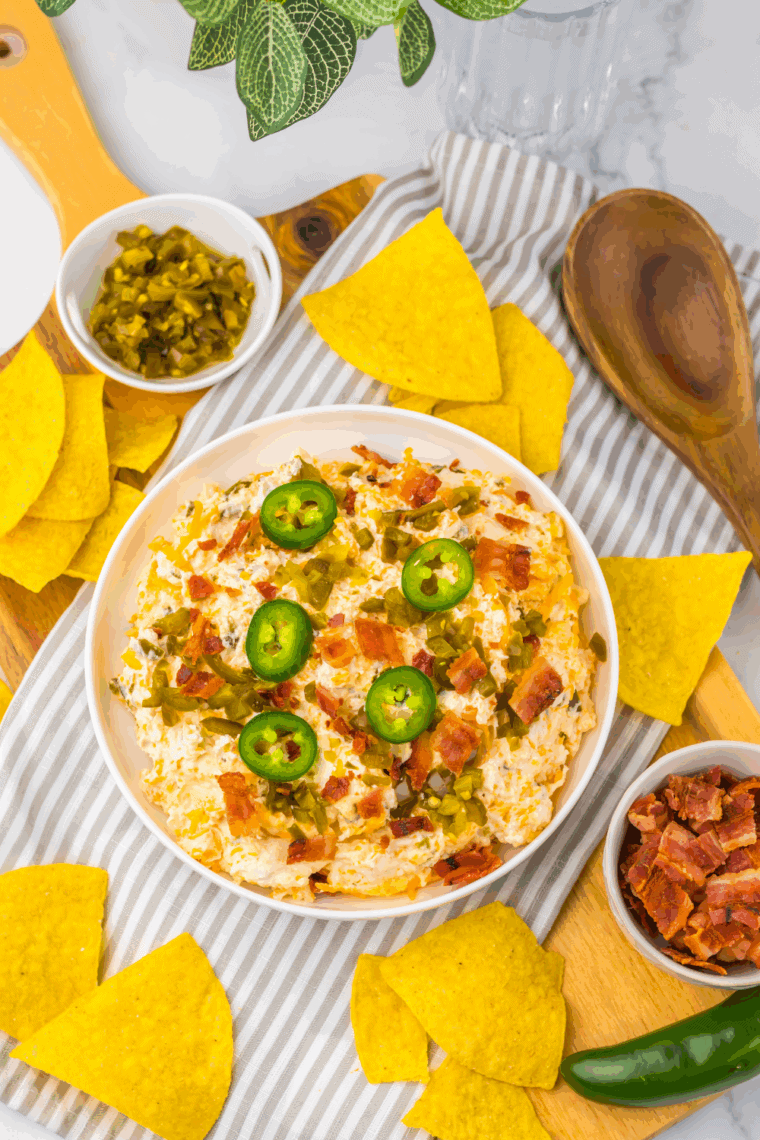 Slow cooker jalape&ntilde;o popper dip topped with bacon, served with chips and crackers