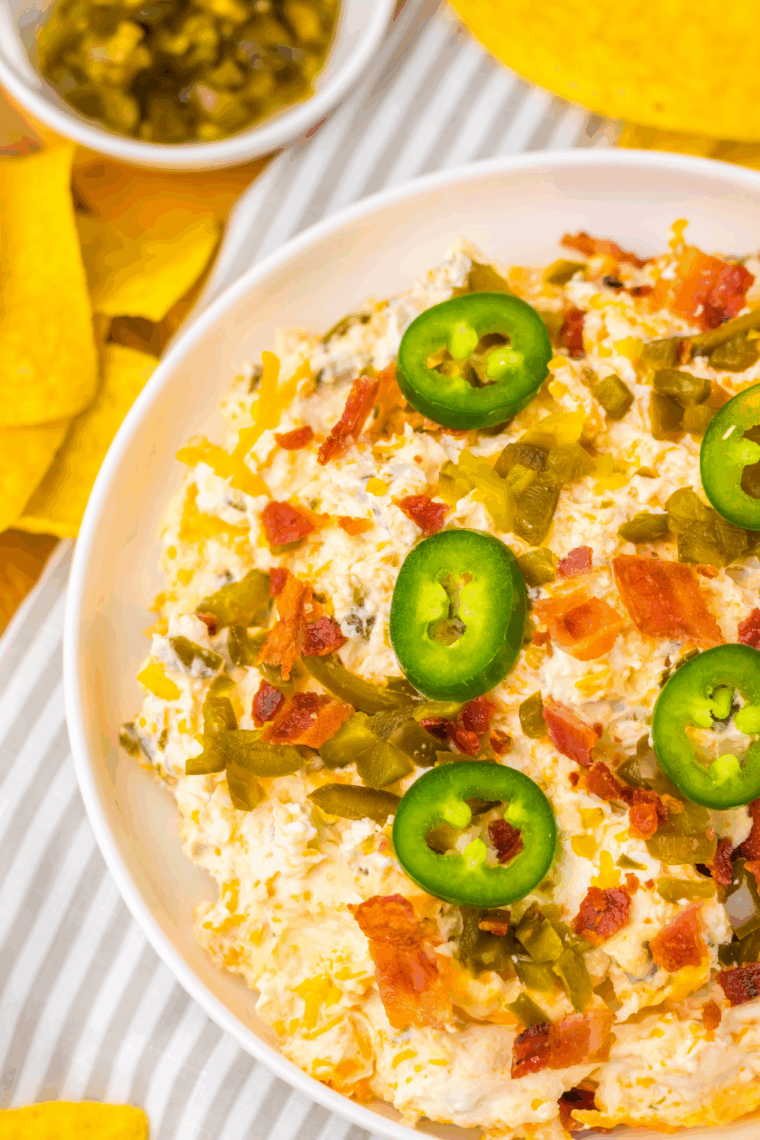 Slow cooker jalape&ntilde;o popper dip topped with crispy bacon, melted cheddar, and jalape&ntilde;os, served with tortilla chips