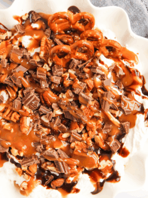 Bowl of Easy Turtle Cheesecake Dip topped with chocolate drizzle, caramel, and chopped pecans.