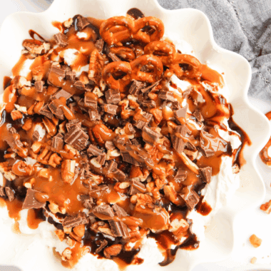 Bowl of Easy Turtle Cheesecake Dip topped with chocolate drizzle, caramel, and chopped pecans.