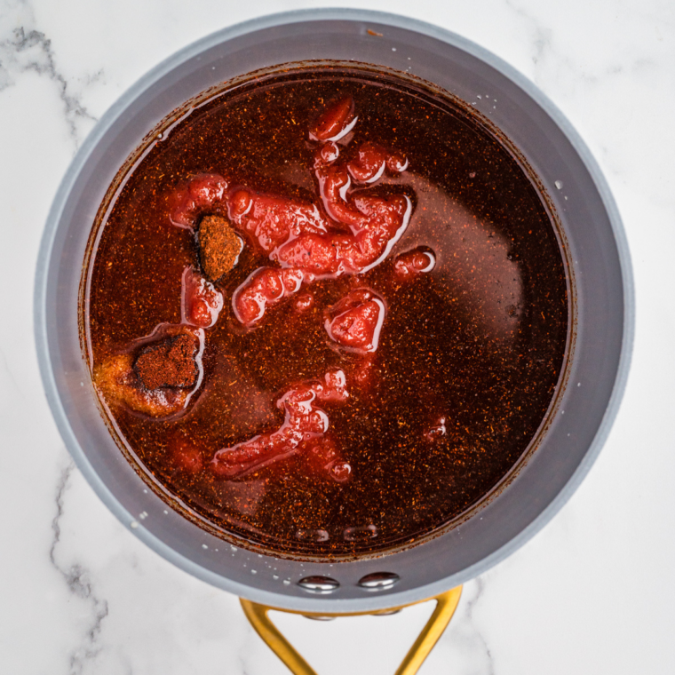 All ingredients for hot honey BBQ sauce in a saucepan before cooking, with ketchup, hot honey, and spices unmixed