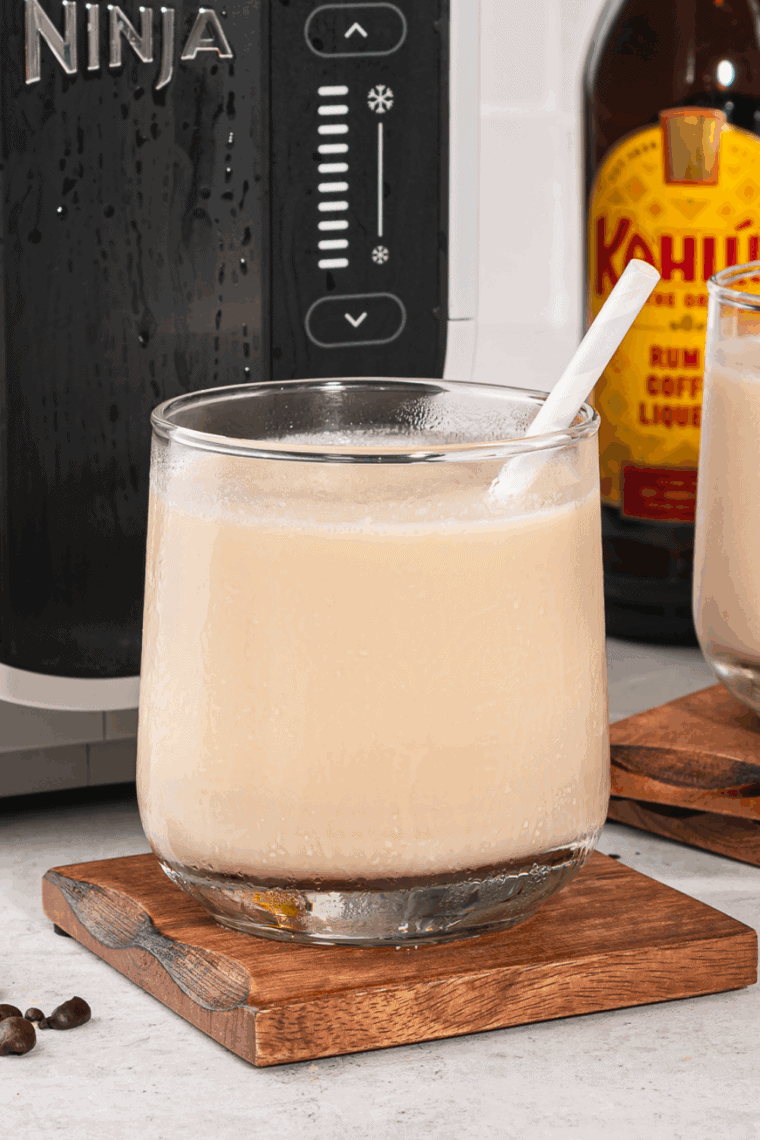 Glass of frozen White Russian slushy made with vodka, Kahl&uacute;a, and milk, served in a clear glass with a straw.