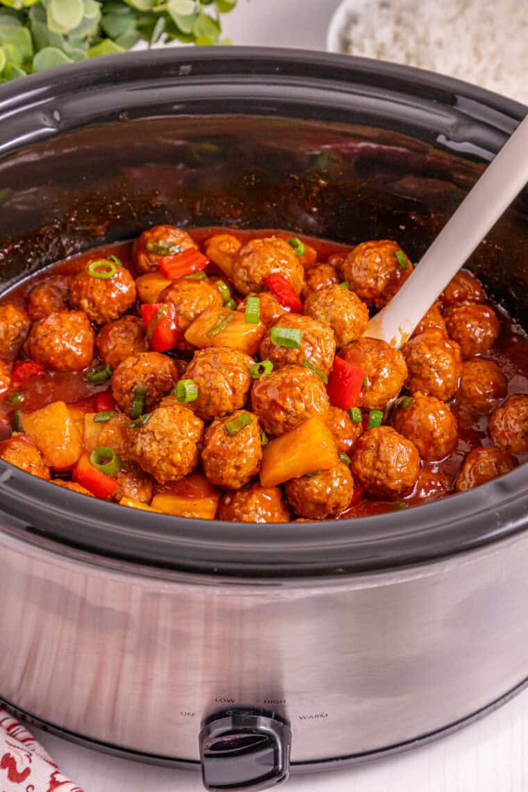 Slow cooker Hawaiian meatballs with pineapple chunks, red bell peppers, and green onion garnish in a sweet BBQ sauce.