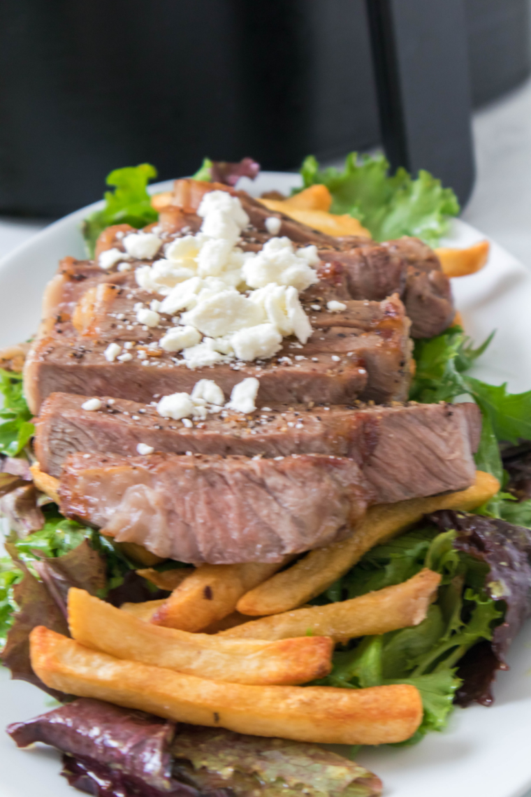 Juicy air fryer steak served with crispy golden fries and a side salad, garnished with fresh herbs.