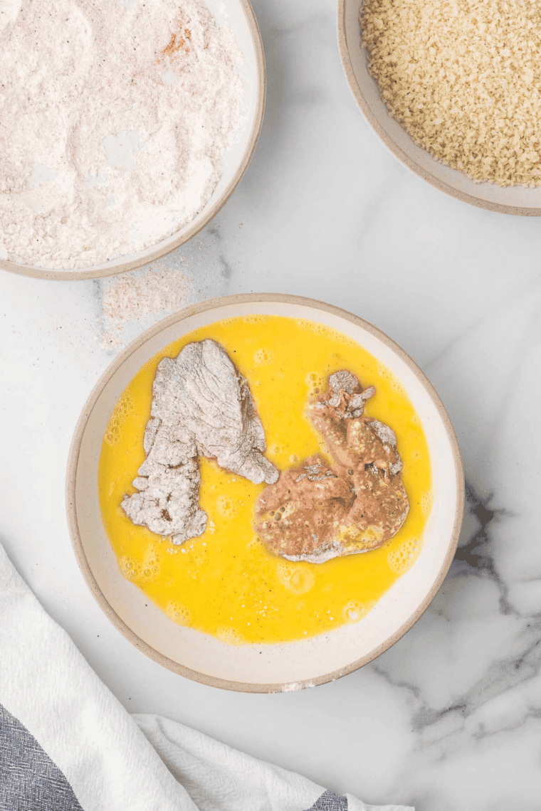 Set Up Breading Station: Three bowls with seasoned flour, beaten eggs, and breadcrumbs ready for breading.