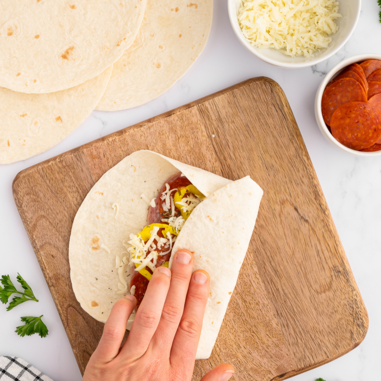 Tortilla being rolled into a tight Italian wrap, keeping fillings inside.
