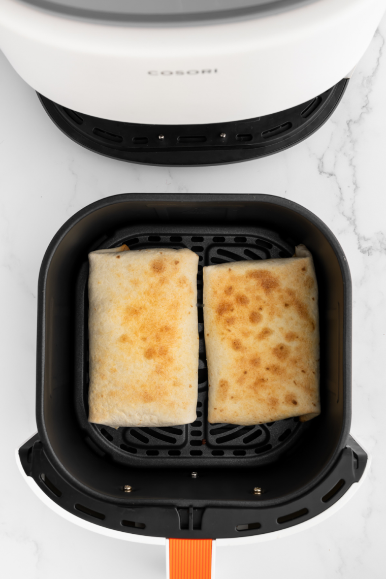 Italian wraps cooking in air fryer basket, turning golden brown, cheese melted.