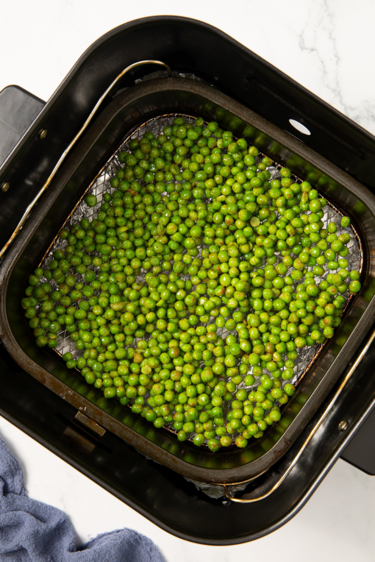 Seasoned peas spread in a single layer in the air fryer basket