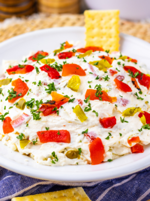 Creamy cream cheese pepper dip served in a bowl with crackers and fresh vegetables on the side.