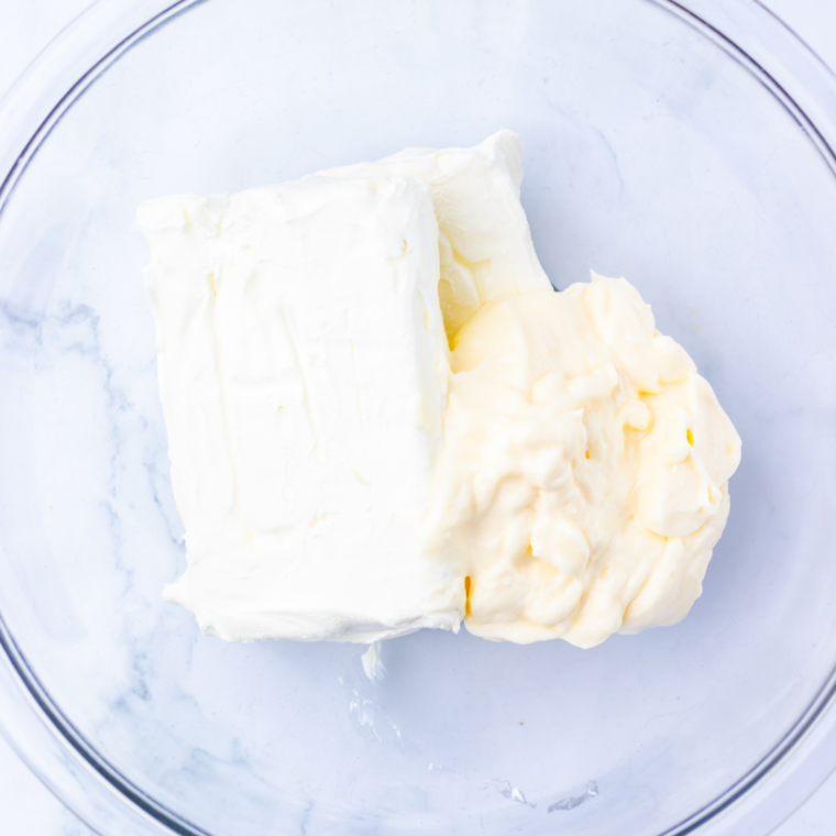 Cream cheese and mayonnaise being mixed in a bowl with a hand mixer, seasoned with onion powder and garlic salt.