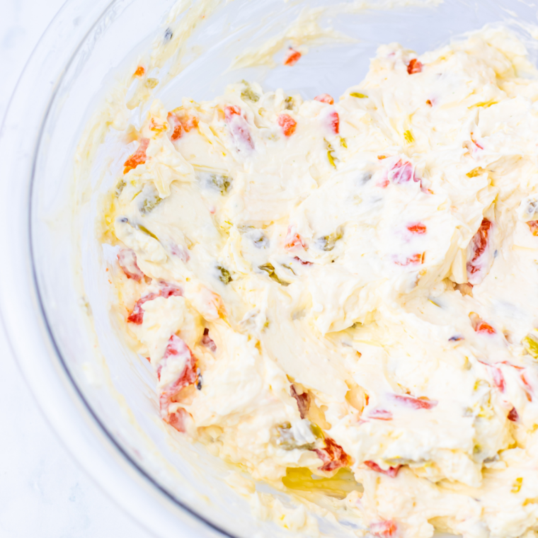 Cream cheese pepper dip served in a bowl with crackers and fresh veggie sticks for dipping.