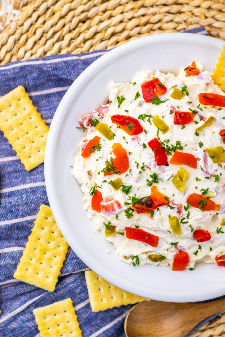 Cream cheese pepper dip served in a bowl with fresh vegetables and crackers for dipping.