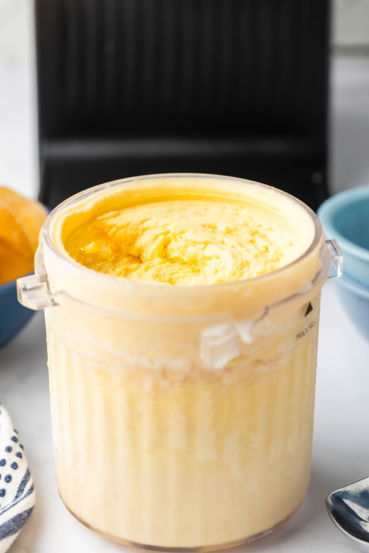 A white plate holding a generous scoop of vibrant orange peach gelato with a smooth, creamy texture.