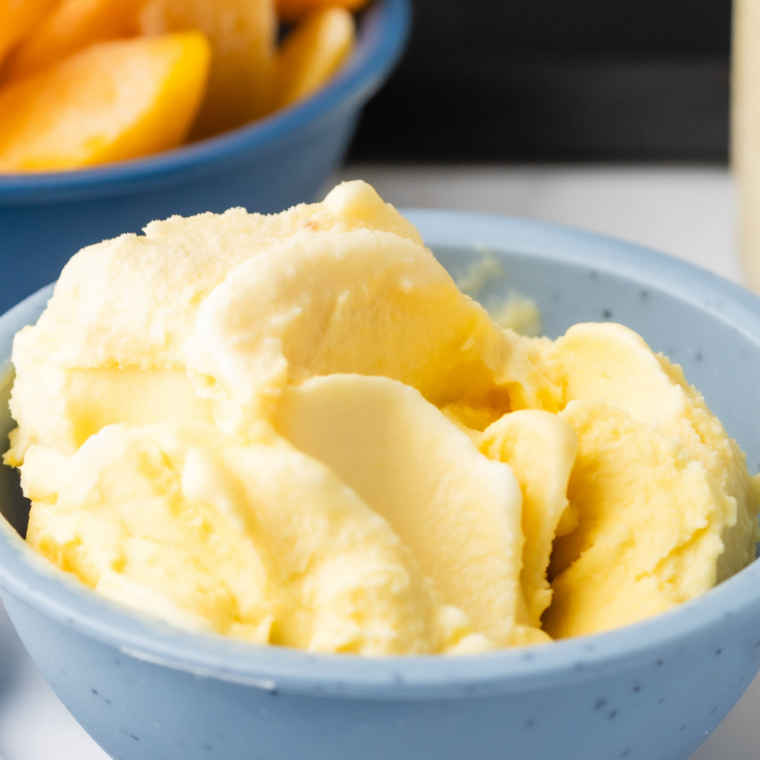 A vibrant scoop of peach gelato served in a bright blue bowl, showcasing a smooth and velvety texture.