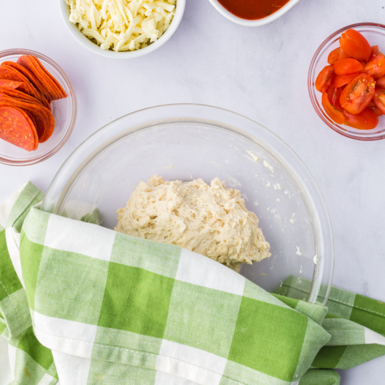 Food processor with high-protein flour, instant yeast, and water forming a rough pizza dough ball.