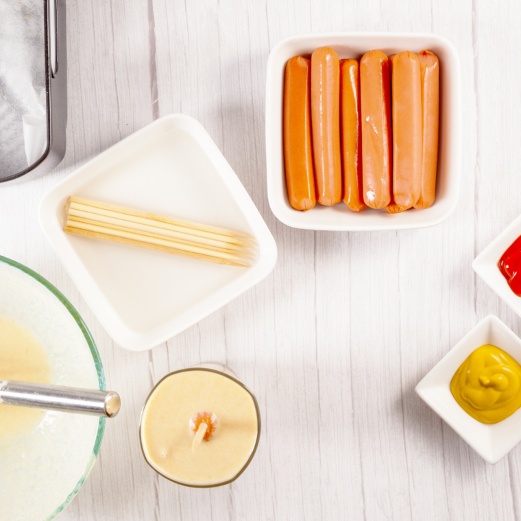 Wooden skewer inserted into hot dog and dipped in cornbread batter.