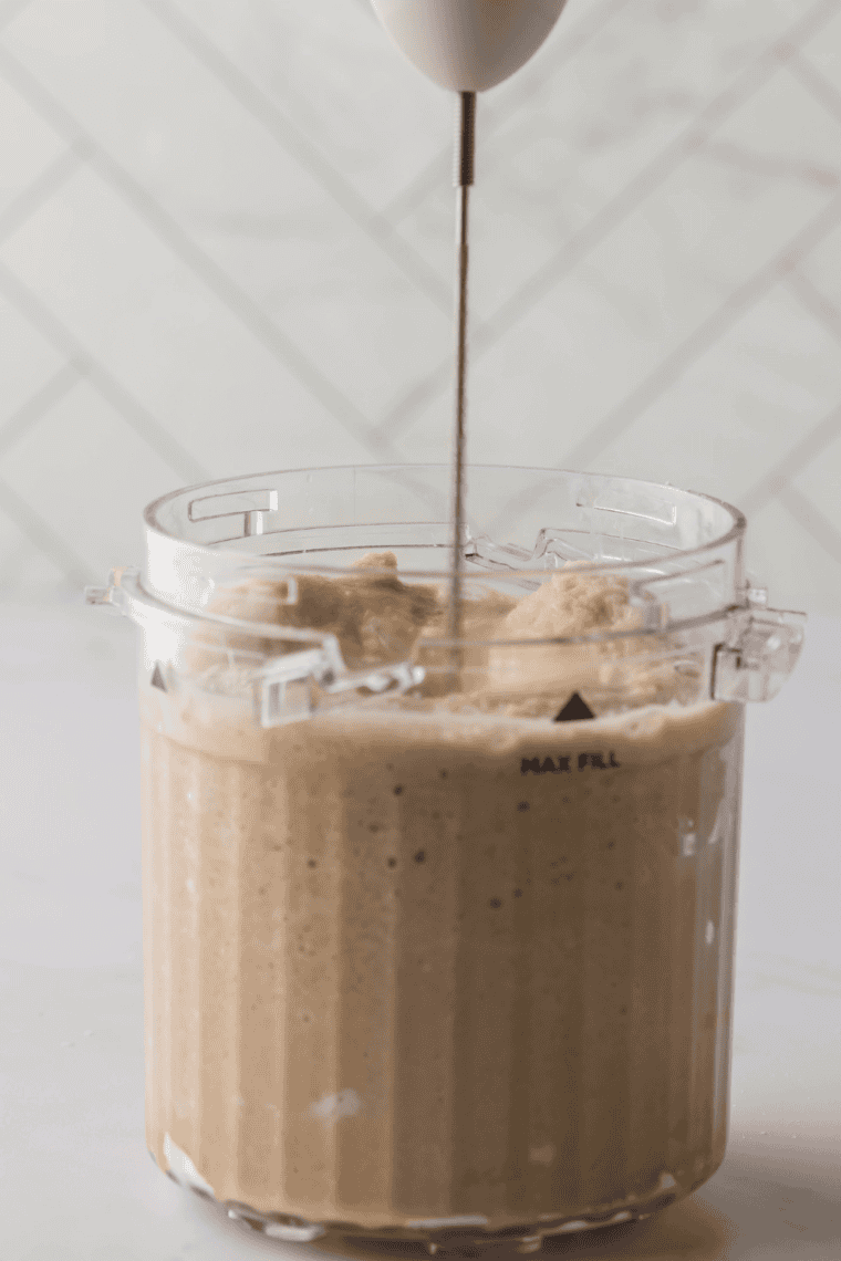 Pouring White Chocolate Mocha Frappuccino&reg; mixture into a Ninja Creami pint, folding in white chocolate chips.
