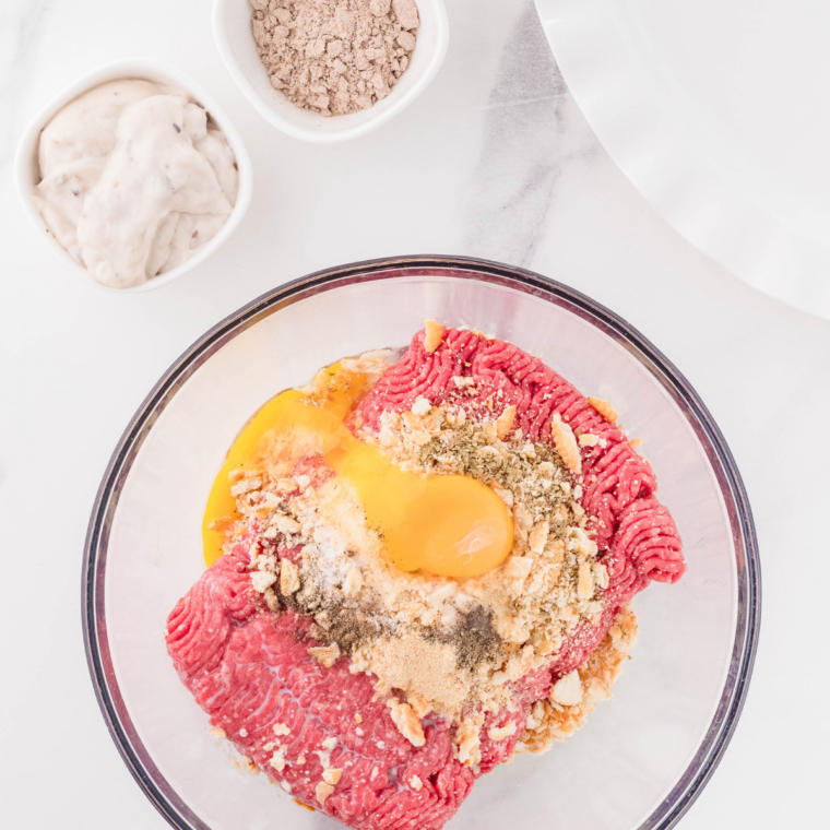 Raw ground beef mixed with seasonings and breadcrumbs in a bowl, shaped into uniform patties.