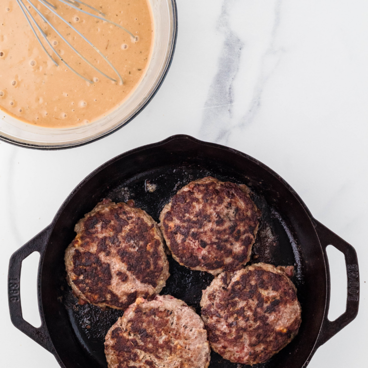 Salisbury steak patties sizzling in a skillet, developing a golden-brown crust.