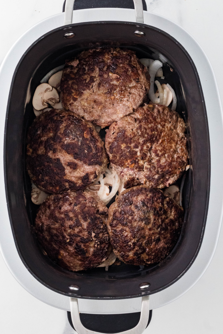 Beef patties arranged in a slow cooker, topped with creamy mushroom sauce.