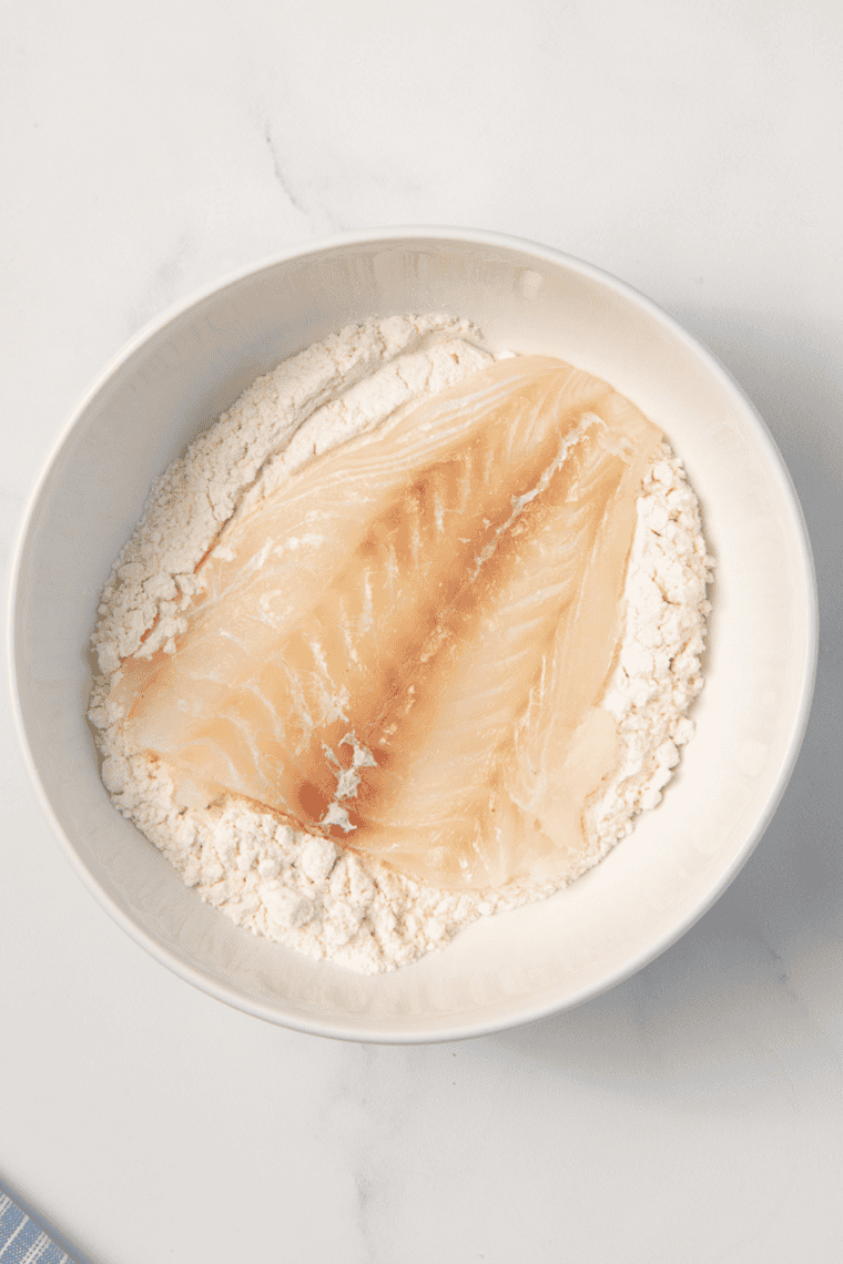 Patting haddock fillets dry with paper towels to remove excess moisture before breading.