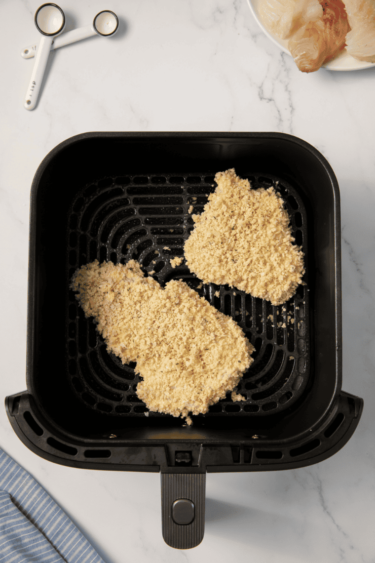 Coated haddock fillets cooking in air fryer at 400&deg;F, golden and crispy, flipping halfway through.