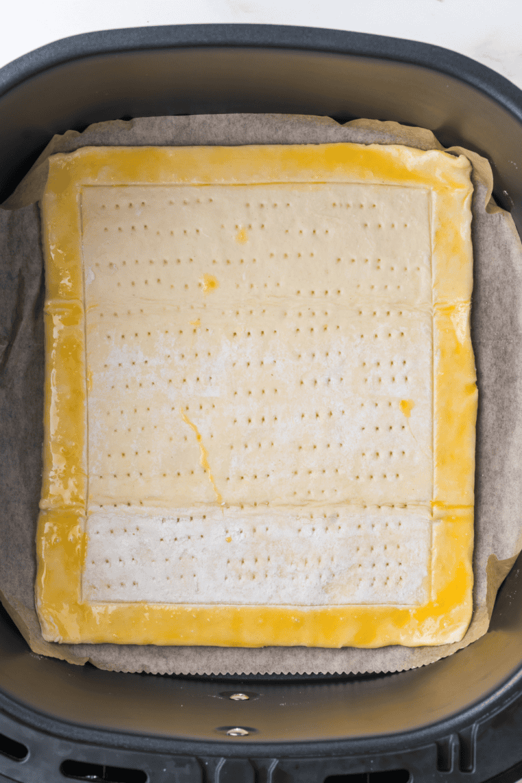 Pastry crust brushed with egg in air fryer basket with parchment paper.