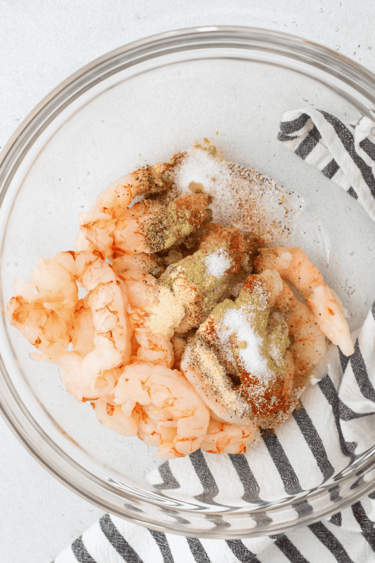 Large bowl with shrimp being coated with spices and olive oil.