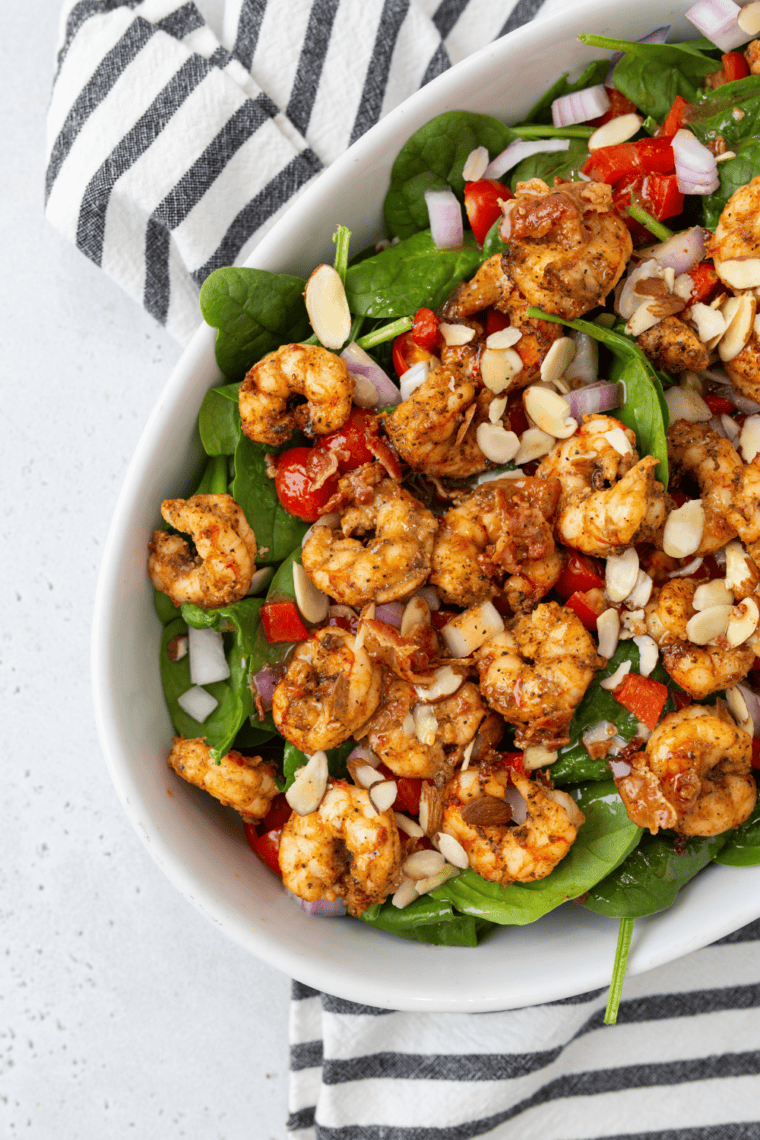 Air fryer shrimp on a bed of fresh spinach with light dressing in a bowl.