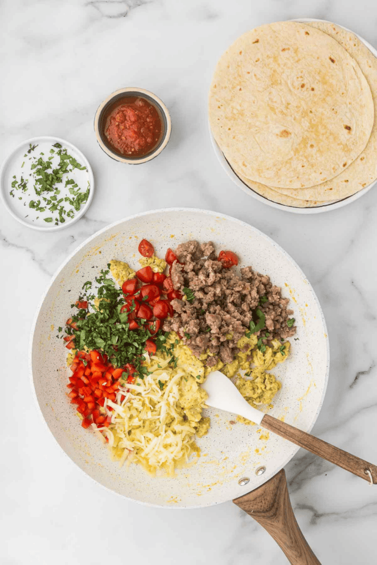 Scrambling with chorizo, cheese, tomatoes, bell peppers, and cilantro in skillet.
