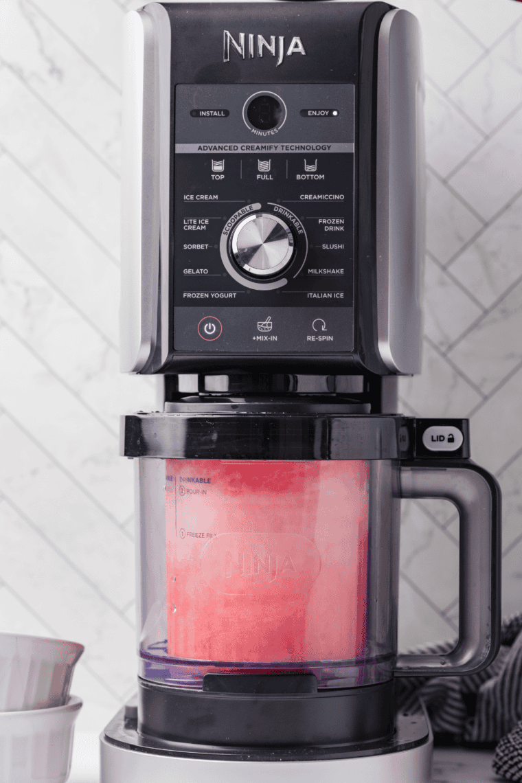 Frozen pint placed in Ninja Creami machine being processed into Italian ice.