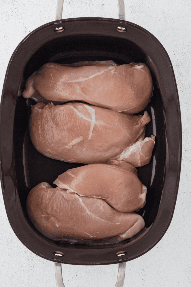 Placing raw chicken breasts in slow cooker before adding sauce.