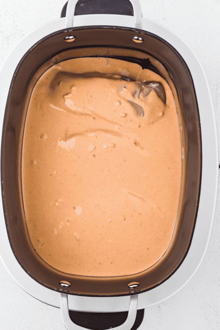 Pouring creamy bang bang sauce over chicken in slow cooker.